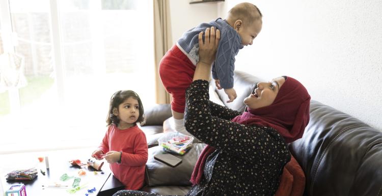 Mother holding up smiling baby with toddler looking on