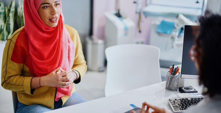 A Muslim woman sits across from her female doctor as she talks with her about cervical cancer