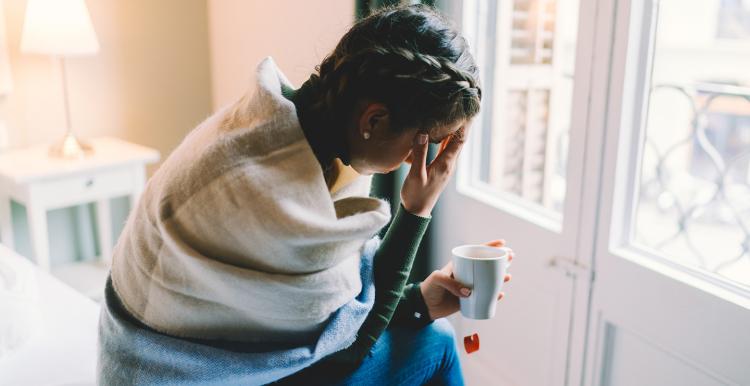 Woman feeling unwell, staying home wrapped in scarf and drinking hot tea