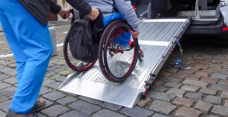 Assistant helping disabled person on wheelchair with transport using accessible van ramp