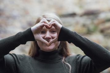 A smiling woman holding up her hands in the shape of a heart