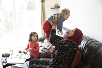 Mother holding up smiling baby with toddler looking on